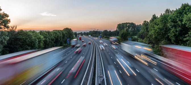 Multi-lane highway with blurred traffic moving at speed through a wooded area.